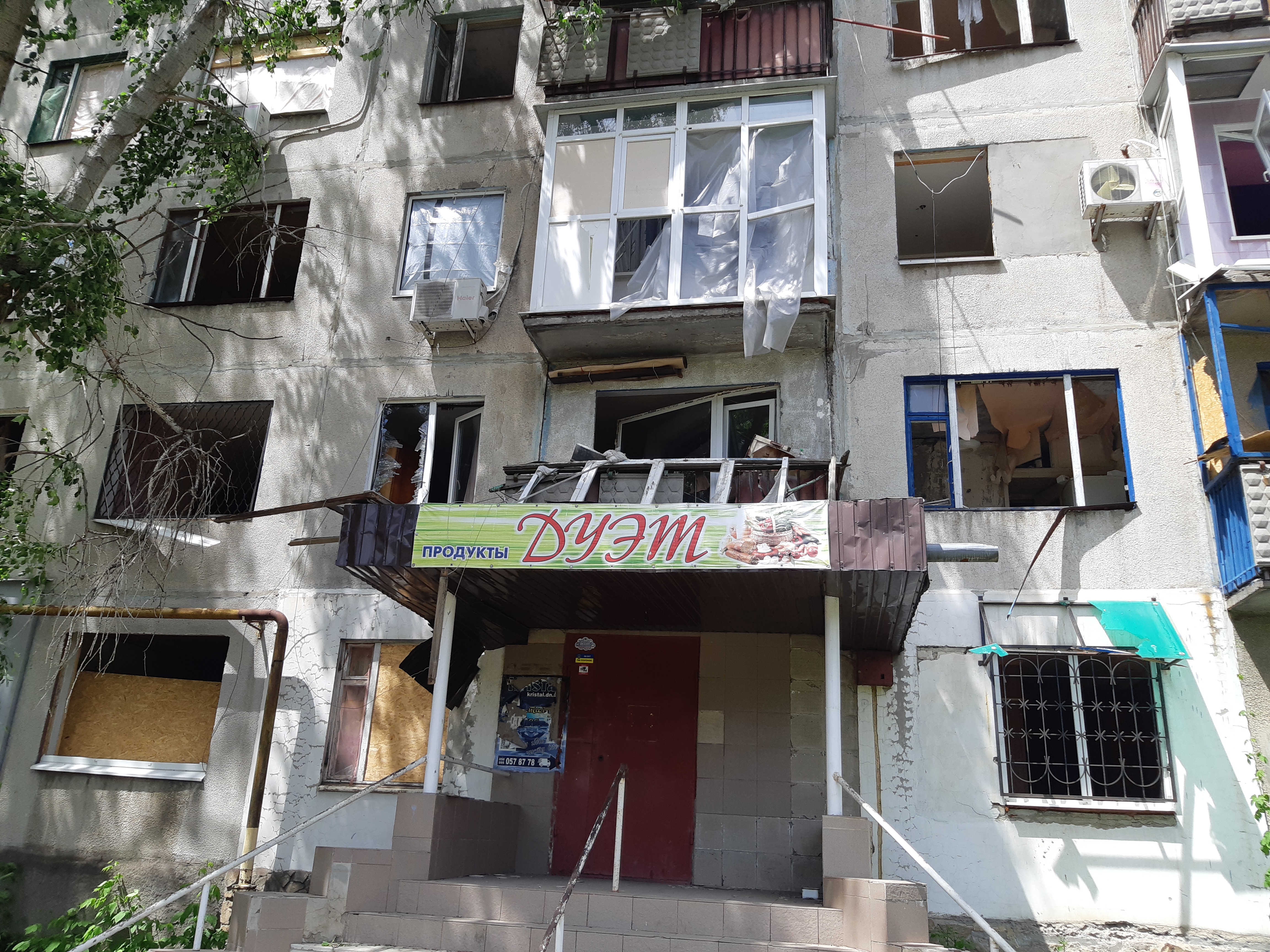 Shell-damaged Soviet-era apartment block with blown-out windows above a Russian-language shop sign, eastern Ukraine. Editor's own photo.