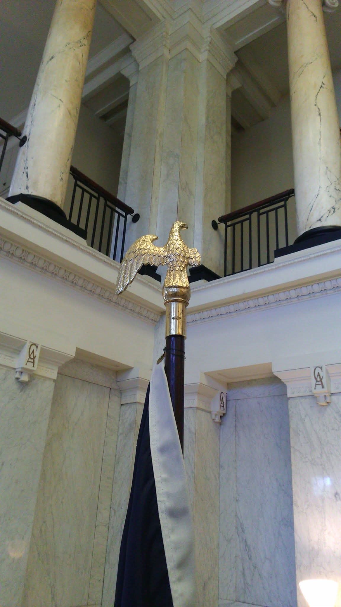 A gilded eagle finial atop a flagpole in a classical marble hall of a U.S. institution
