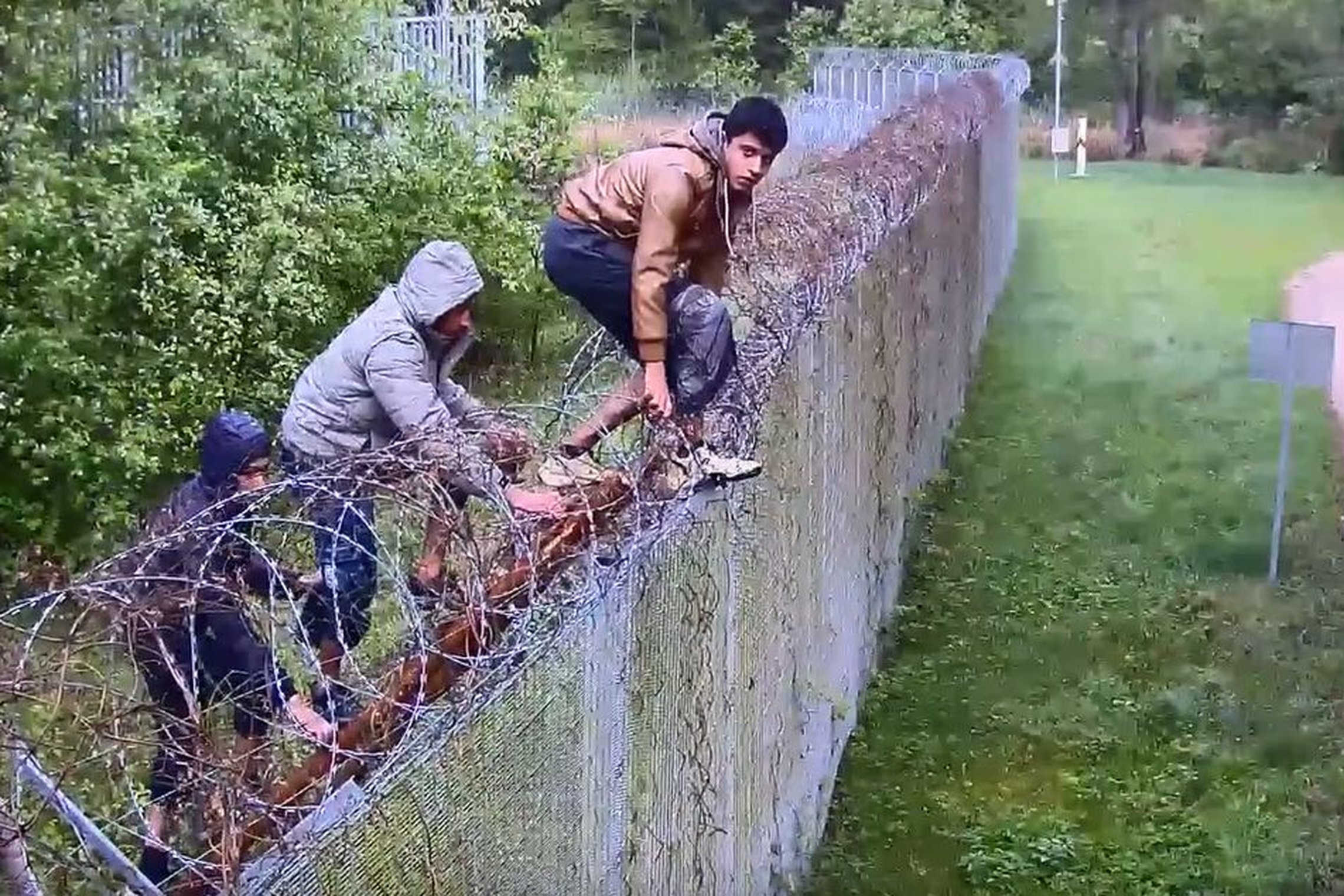 Migrants climb over the razor-wire fence on the Lithuania-Belarus border