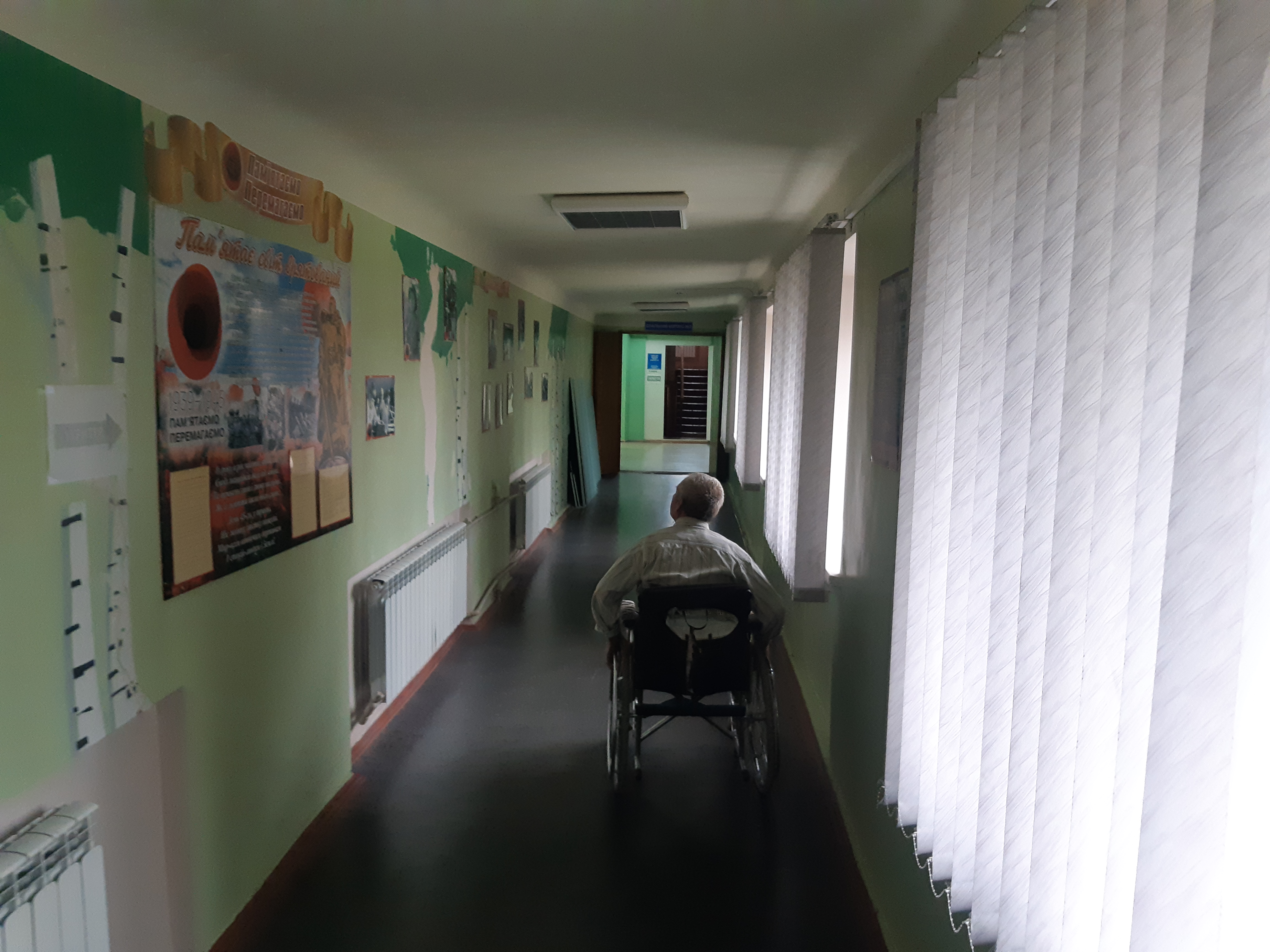 An elderly man in a wheelchair moves down the corridor of a Ukrainian public institution