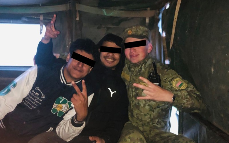Migrants posing with a Belarusian border officer